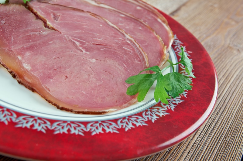 Slices of Hangikjöt (traditional Icelandic smoked lamb) garnished with a sprig of parsley, served on a red and white decorative plate. Hangikjöt is the typical Christmas feast in Iceland.