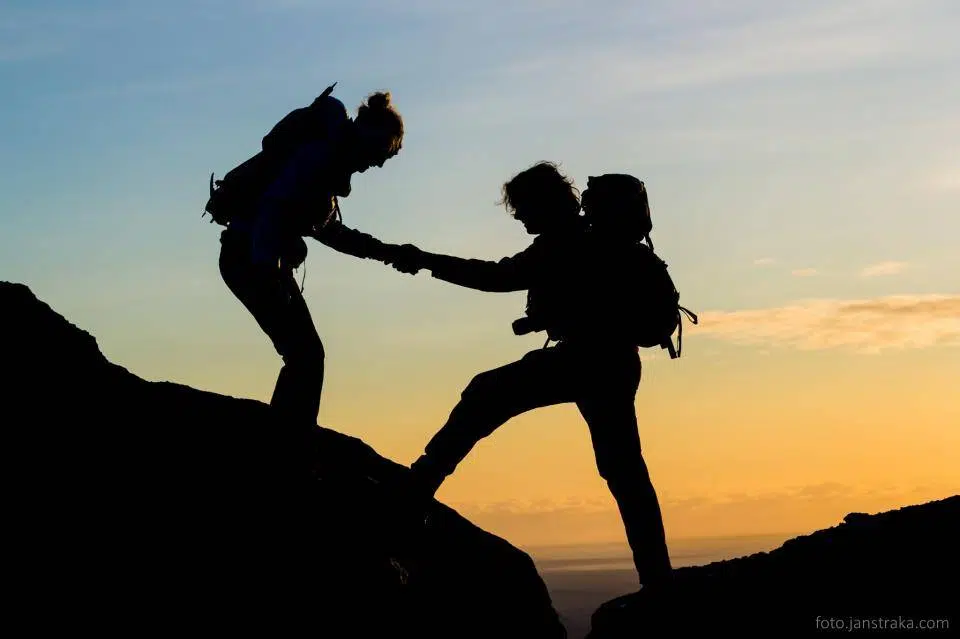 People helping each other hiking in the twilight.