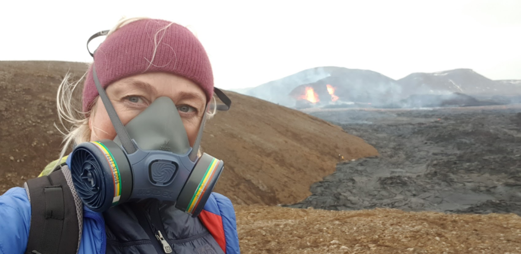 Woman with a mask in front an erupting volcano.