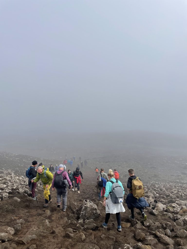 People walking across rocky ground in fog on their way to the volcano erupting in Iceland in 2022