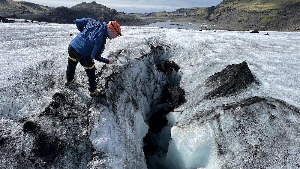 A man on an Icelandic glacier looks into a crevasse.