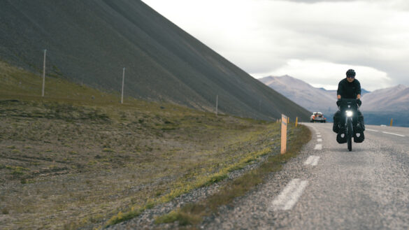 A woman is on the side of the highway in Iceland, cycling around Iceland.