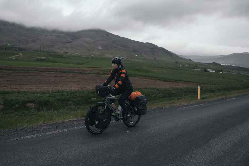 A young woman cycles down a highway in Iceland.