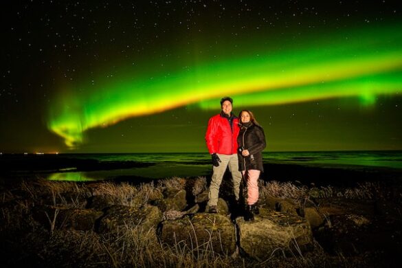 A man and woman standing together in Iceland with the northern lights in the background.