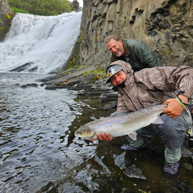 Two men holding a salmon by a river in Iceland.