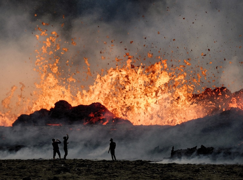 Three men are seen in front of an erupting volcano in Iceland.
