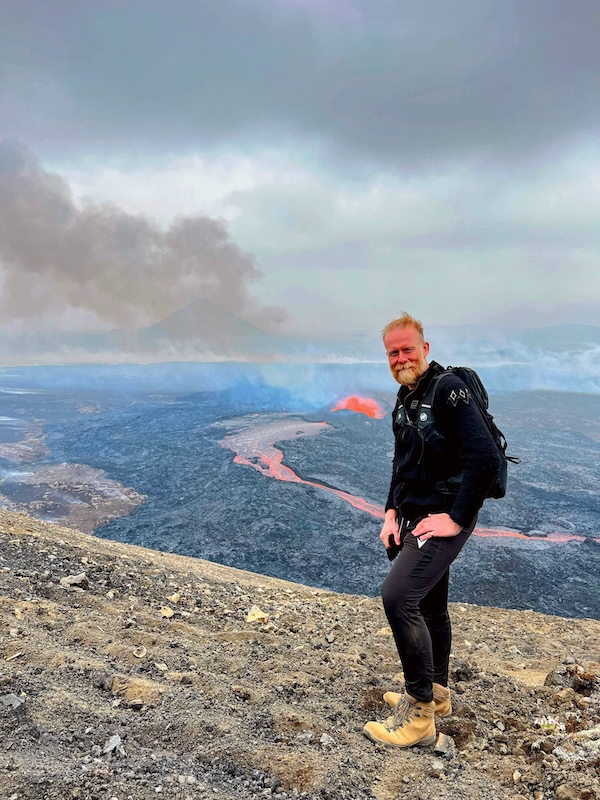 A man stands in front a volcanic eruption in Iceland.