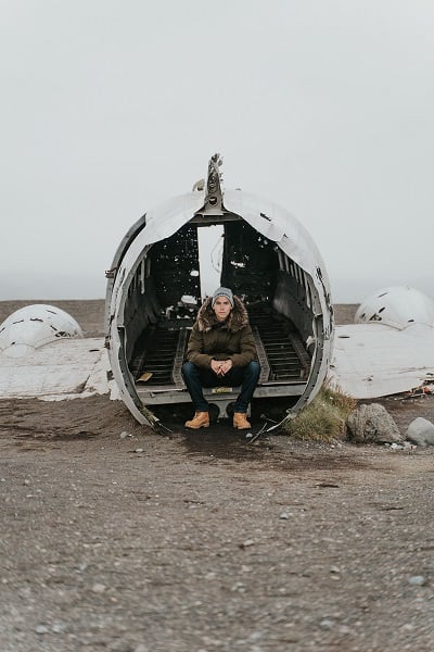 Young man sits on a plane wreck in Iceland.