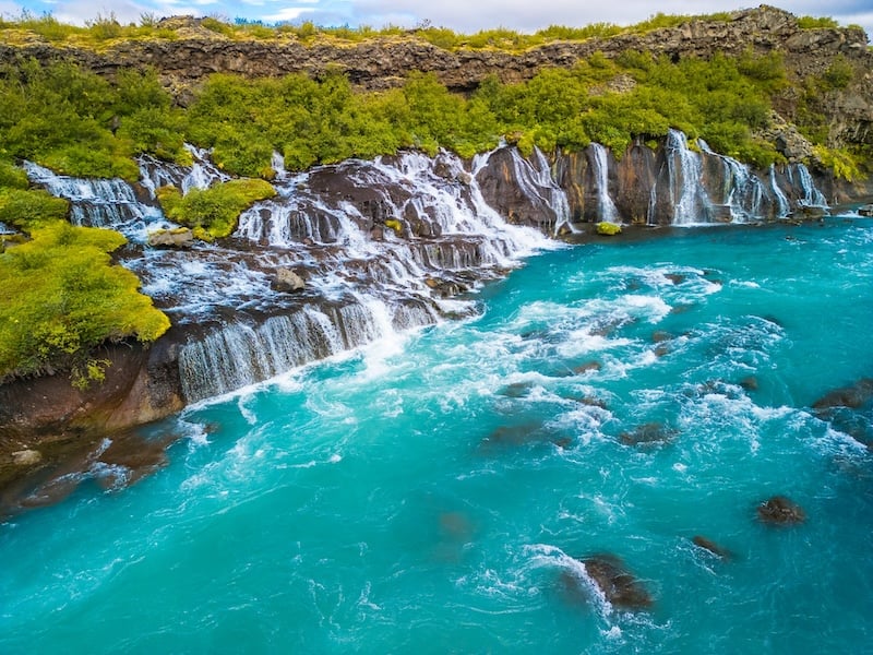 Hraunfossar waterfall in Borgarfjörður, West Iceland, with glacial water streaming from lava rocks into the bright blue Hvítá River, a top attraction on the Silver Circle road trip.