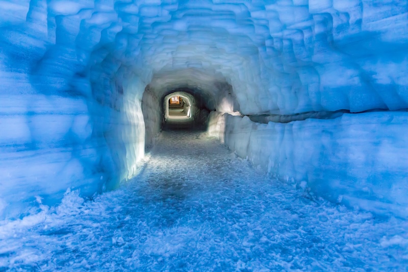 Into the Glacier ice tunnel in Langjökull Glacier, Iceland, featuring illuminated blue ice walls and a frozen walkway, a unique attraction on the Silver Circle route.