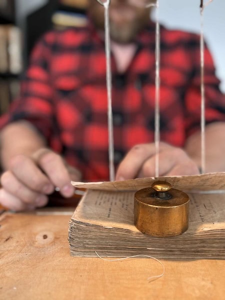 Eyþór Guðmundsson skillfully repairs the spine of an old Icelandic book, using traditional bookbinding tools to preserve its fragile pages for future generations.