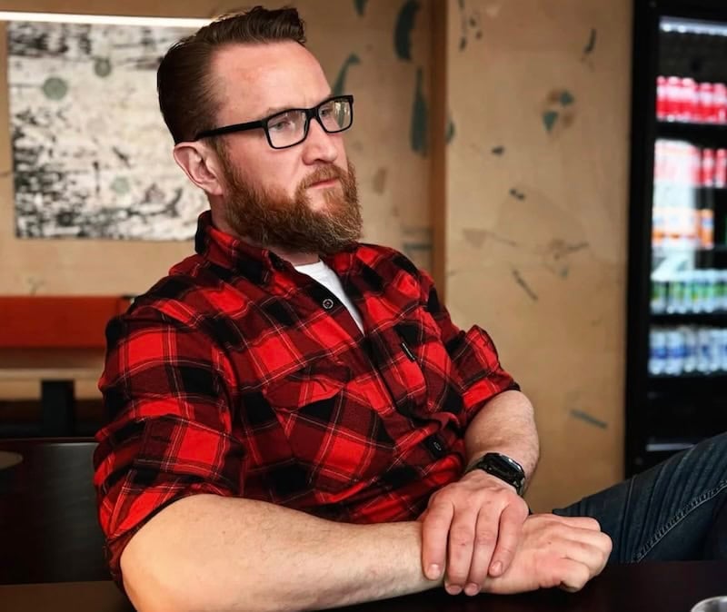 Eyþór Guðmundsson, an Icelandic book collector and restorer, wearing a red plaid shirt and glasses, sits thoughtfully in a cozy setting. He is known for preserving and restoring rare Icelandic manuscripts and books.