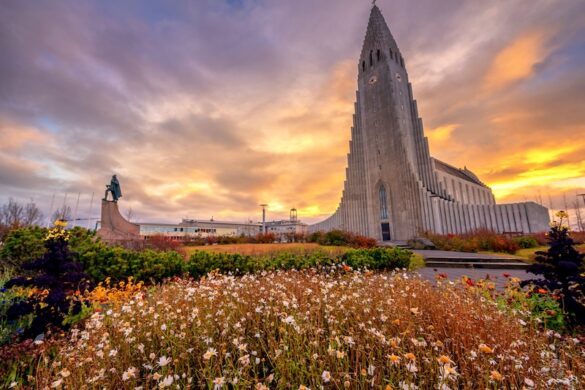 Photo of Hallgrímskirkja church in Reykjavík, Iceland, at sunset with vibrant autumn flowers and the Leifur Eiríksson statue in the foreground.