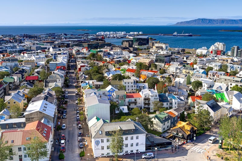 Breathtaking view over Reykjavík from the top of Hallgrímskirkja, capturing the vibrant cityscape, harbor activity, and the distant Mount Esja under a bright Icelandic summer sky.