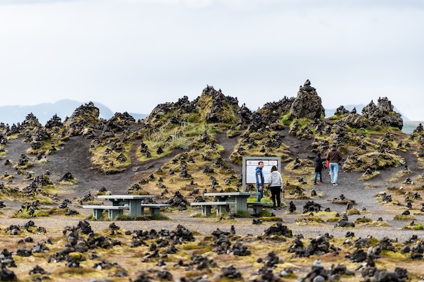 Laufskálavarða, a famous site of cairns in Iceland, featuring countless stone piles across a mossy volcanic landscape with visitors exploring the area.