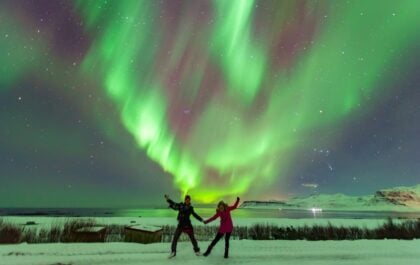 Two travelers enjoying the Northern Lights in Iceland during winter. Discover the best campervan deal for Iceland winter travel and explore the country’s stunning snowy landscapes at your own pace.