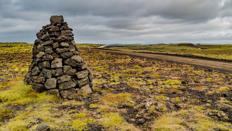 A solitary historic cairn in Iceland marks the way across a vast lava field, echoing the traditions of ancient travelers.