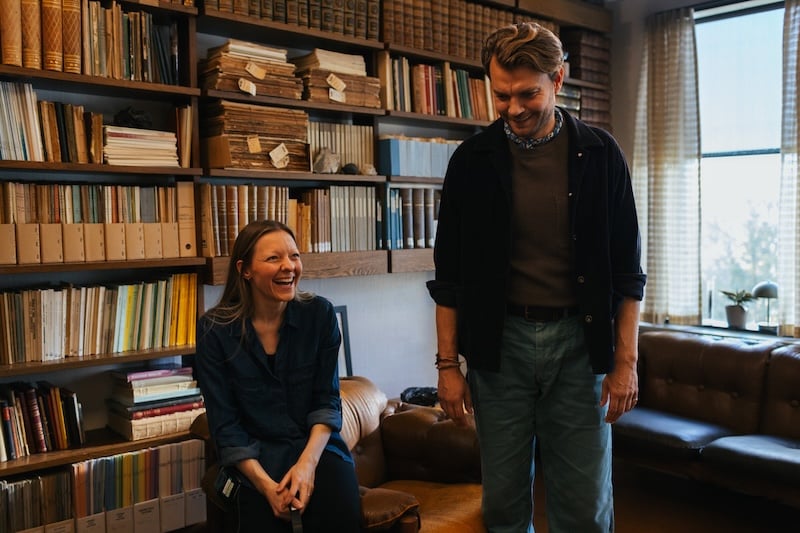 Director Ugla Hauksdottir and actor Pilou Asbæk sharing a laugh on the set of The Fires, inside a cozy, book-filled room.