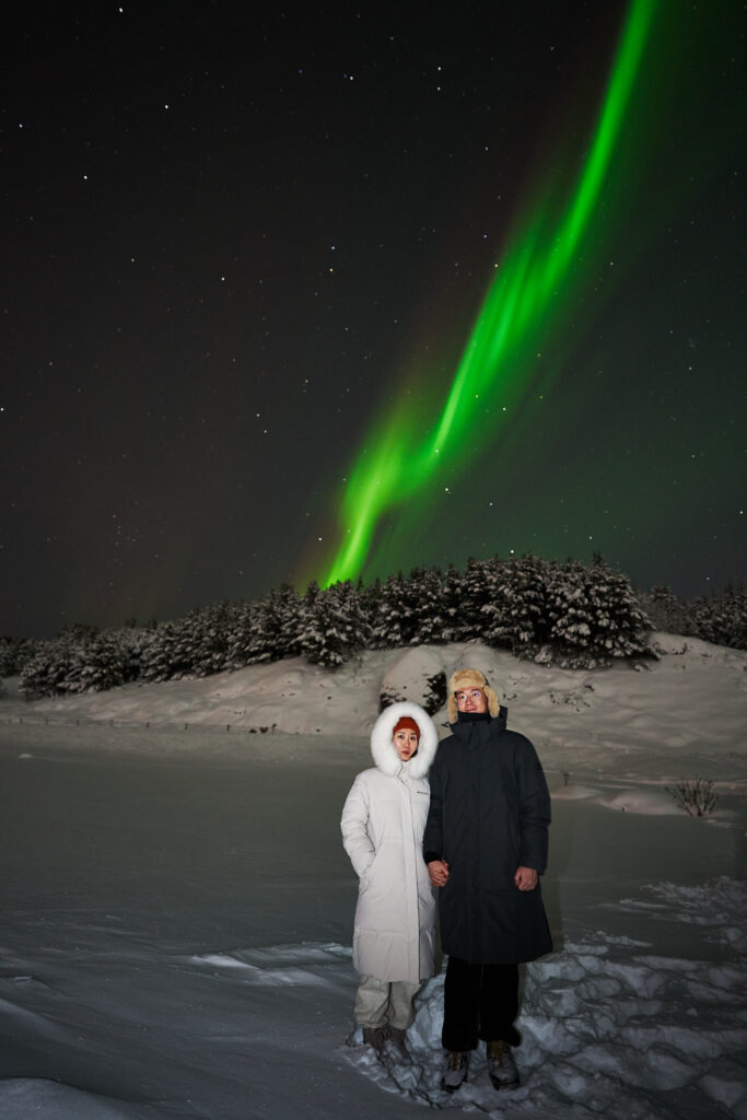 A couple in overcoats are shown underneath the northern lights in Iceland in winter.