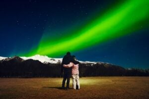 Couple watching the Northern Lights in Iceland with snow-covered mountains in the background on a clear winter night.