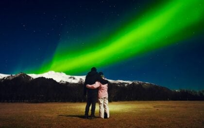 Couple watching the Northern Lights in Iceland with snow-covered mountains in the background on a clear winter night.