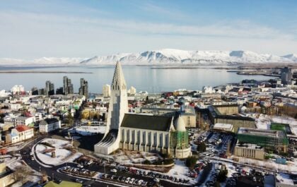 Aerial view of Reykjavík in winter showing Hallgrímskirkja church, snowy streets, Faxaflói Bay, and Mount Esja under clear skies.