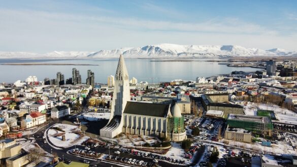 Aerial view of Reykjavík in winter showing Hallgrímskirkja church, snowy streets, Faxaflói Bay, and Mount Esja under clear skies.