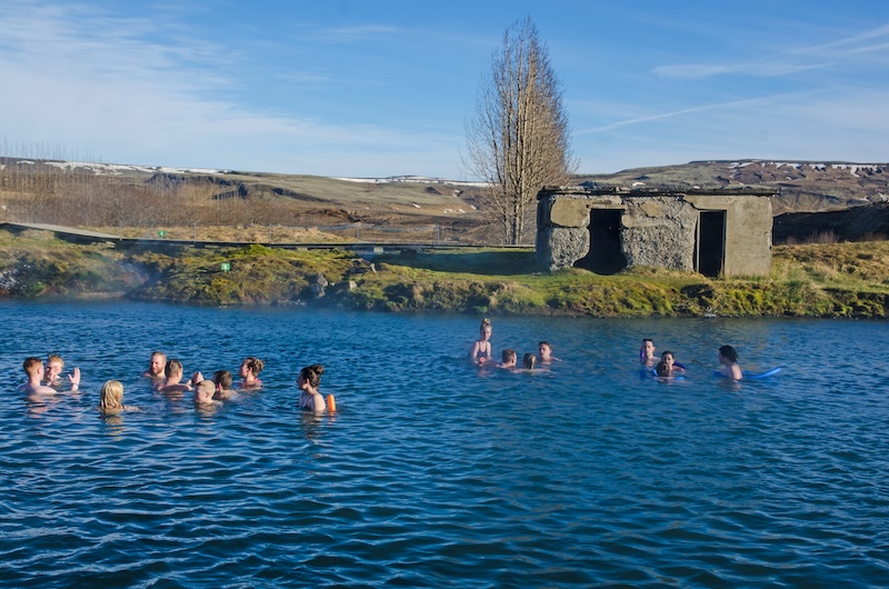 Visitors bathing in Secret Lagoon natural hot spring with steaming geothermal water and historic stone building near Fludir on Iceland's Golden Circle