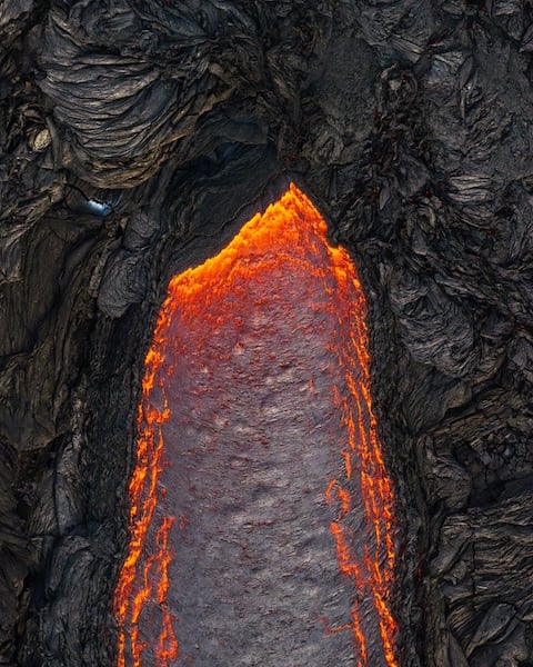 Aerial drone view of active lava flow through black basalt Reykjanes Peninsula Iceland - Rico de Jong.