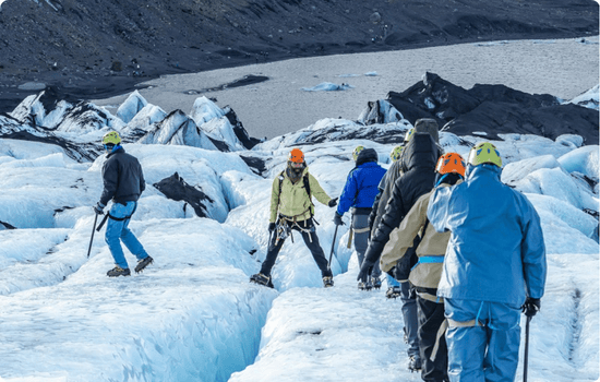 Group of travelers hiking across a glacier in Iceland, wearing helmets and crampons, surrounded by blue ice formations and rugged volcanic scenery.