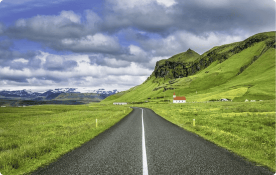 Empty paved road cutting through green countryside in Iceland, capturing the open landscapes and freedom of an Iceland road trip vacation.