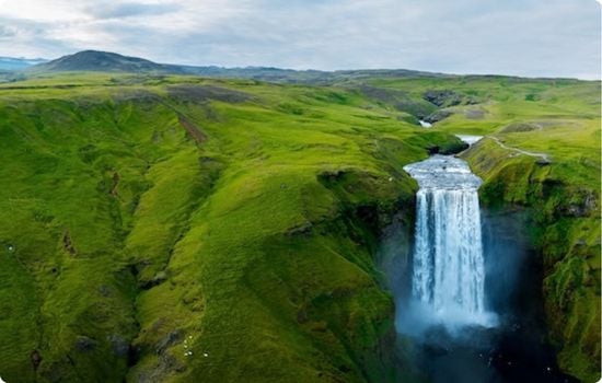 Skógafoss waterfall on Iceland’s south coast, with a wide curtain of water plunging from a green cliff into a misty pool below.