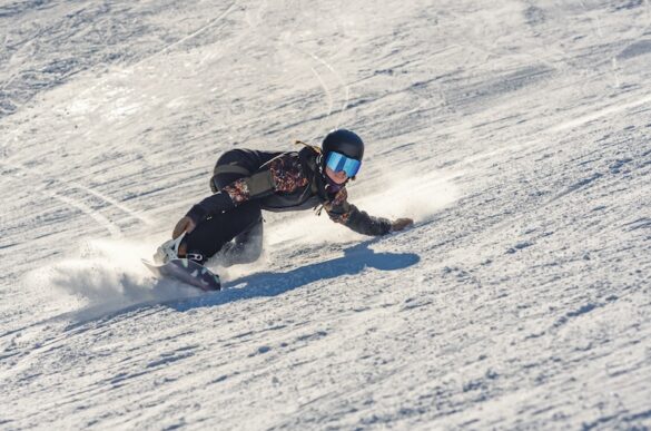 Snowboarder carving sharply down a snowy mountain slope in Iceland on a sunny winter day, showcasing an exciting Iceland snowboarding adventure.