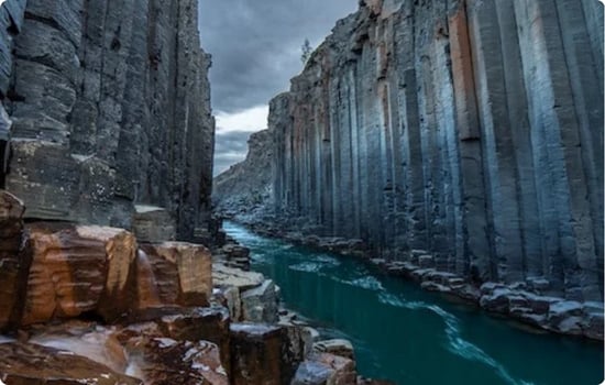 Basalt column canyon at Stuðlagil in East Iceland, with tall hexagonal rock walls and a turquoise glacial river flowing through the narrow gorge.