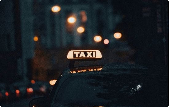 Illuminated taxi sign on a car at night, with blurred city lights in the background, representing airport transfers and taxi services in Iceland.