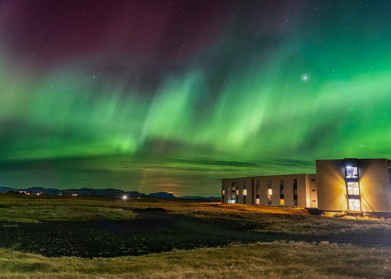 Northern Lights aurora borealis dancing over Landhotel in South Iceland with green aurora curtains illuminating night sky near Hella