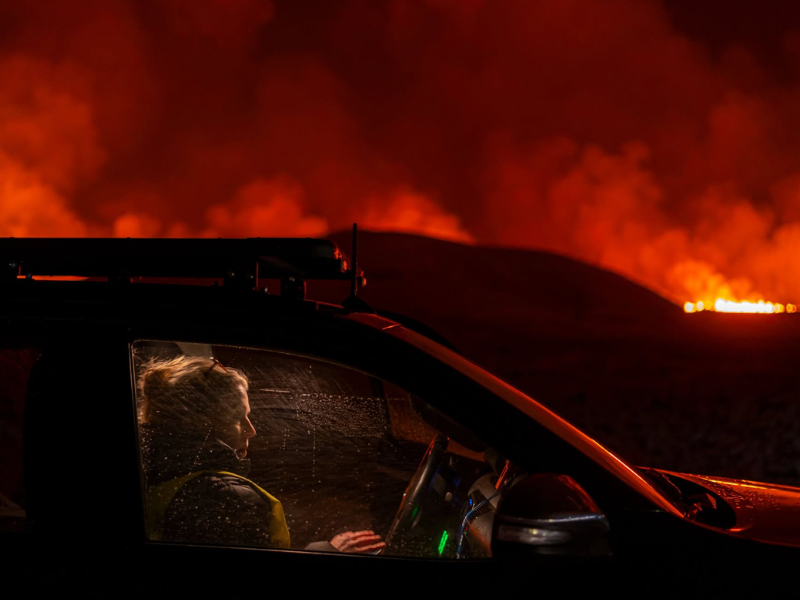 Icelandic author, and reporter Sigríður Hagalín Björnsdóttir She is sitting in a car. In the background is a fiery volcanic eruption.Photo by Golli.