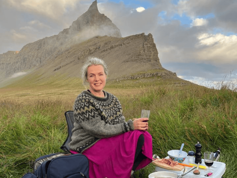 Icelandic author Sigríður Hagalín Björnsdóttir wearing traditional Icelandic wool sweater at outdoor picnic with dramatic mountain peak in background Iceland