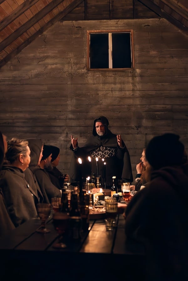 Storyteller Valdimar Flygenring gesturing while telling Njál's Saga to guests seated at a candlelit table in a rustic barn at Mr. Iceland farm.
