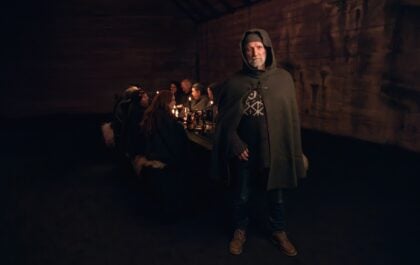 Storyteller Valdimar Flygenring in a hooded wool cape standing before guests at a candlelit Viking Story Night at Mr. Iceland, Hvolsvöllur