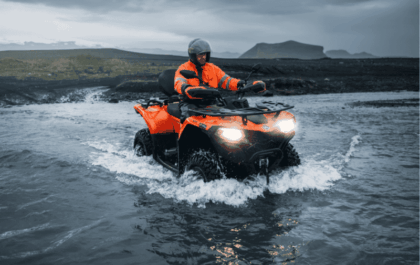 Guide on an orange ATV crossing a glacial river in south Iceland on an Icelandic Mountain Guides tour, headlights on.