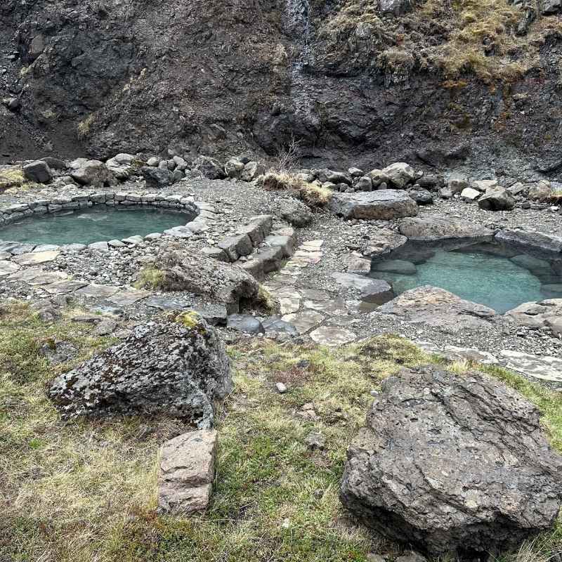 Two stone-built geothermal pools at Canyon Baths near Hotel Húsafell, set against a mossy canyon wall with a small waterfall.
