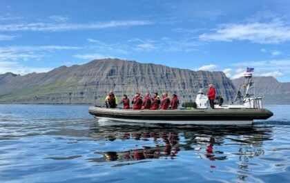 RIB boat with guests and skipper crossing mirror-calm water below steep fjord mountains