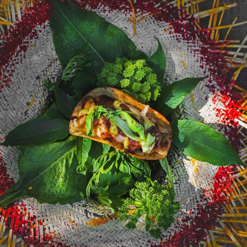 Taco Verde from La hamaca y la luna in Seyðisfjörður, served on a bed of fresh green herbs inside a colorful woven Paraguayan straw hat with red and yellow fringe.