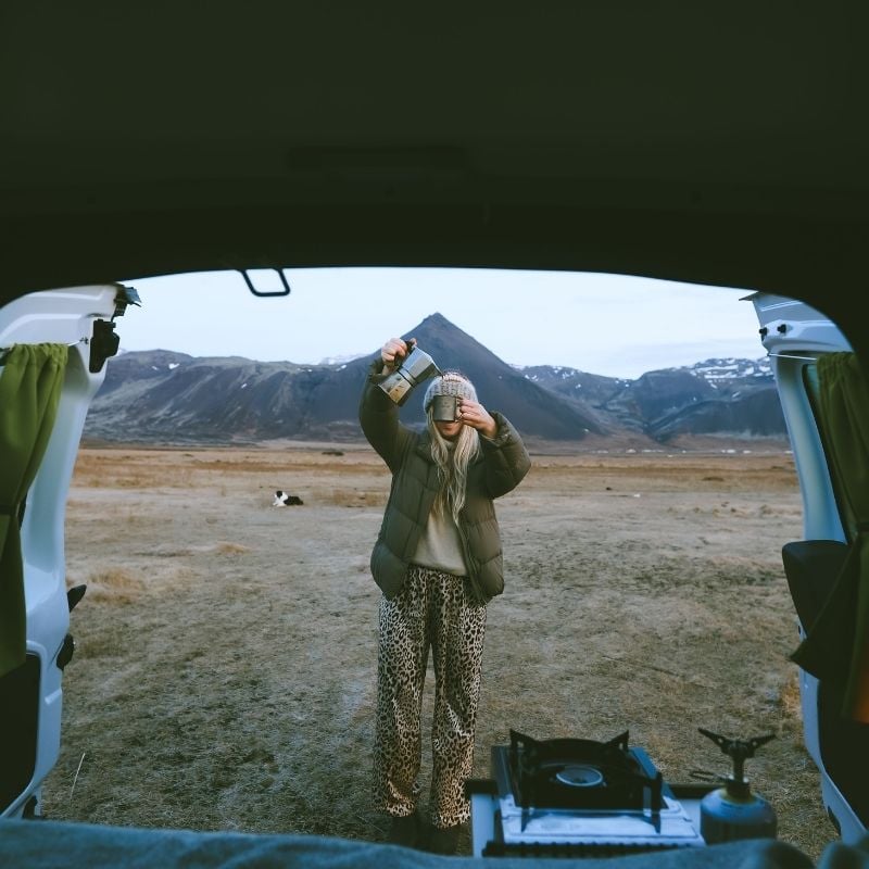 Traveller pouring morning coffee from a moka pot beside a camping stove, seen from inside a Go Campers campervan on the Snæfellsnes Peninsula in Iceland. Photo credit: Go Campers.