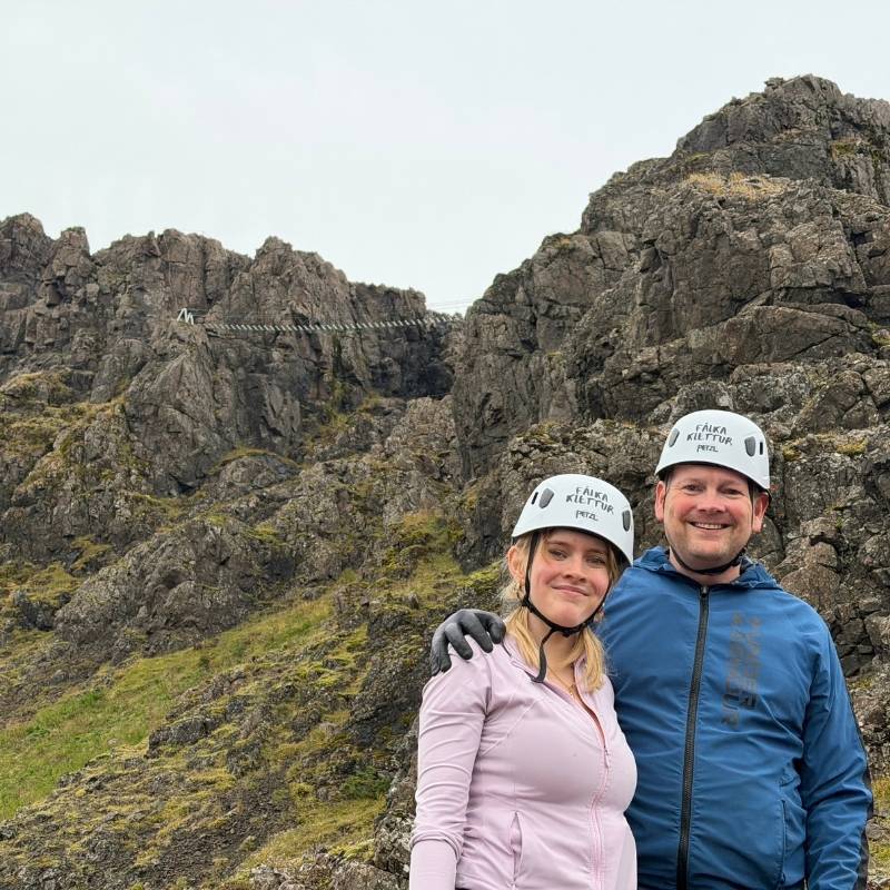 Jon Ragnheidarson, the editor of Stuck in Iceland Travel Magazine and his daughter Ragnheiður in climbing helmets, with the Fálkaklettur suspension bridge on the ridge behind them.
