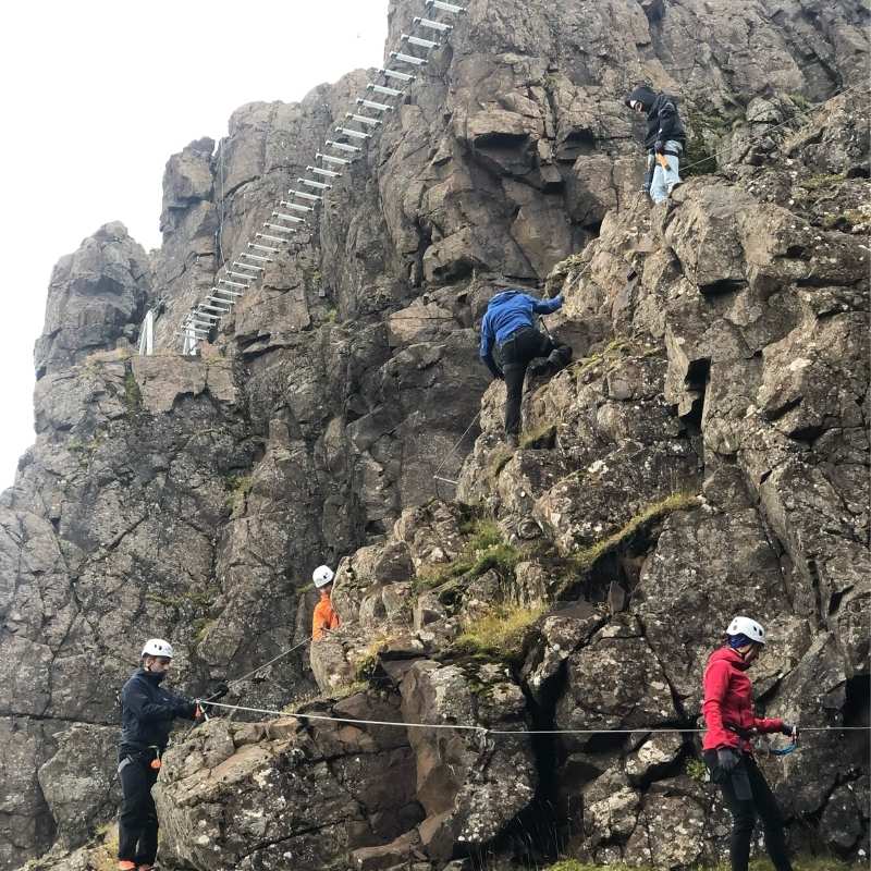 Climbers spread across the Fálkaklettur via ferrata on Mt. Esja, with a run of metal rungs on the rock face behind them.